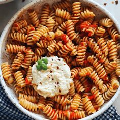 a bowl filled with pasta and sauce on top of a blue checkered cloth next to a spoon