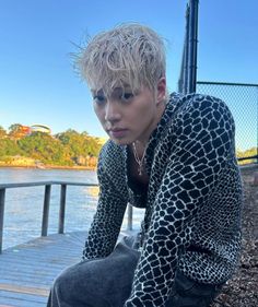 a young man sitting on top of a wooden bench next to a body of water