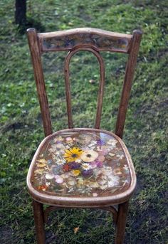 an old wooden chair with flowers painted on it's seat is sitting in the grass