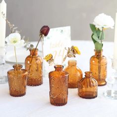 there are many small vases with flowers in them on the tableclothed table