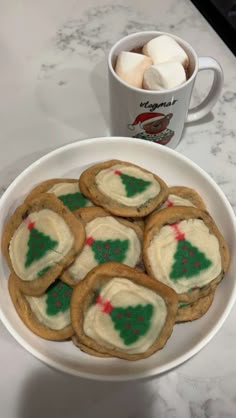 some cookies and marshmallows are on a plate next to a cup of coffee