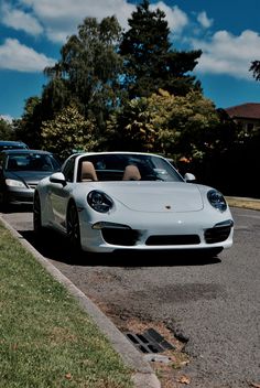 a white sports car driving down a street next to another car on the side of the road