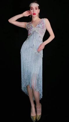 a woman in a dress with fringes on her head and heels standing against a black background