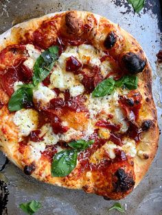 a pizza sitting on top of a pan covered in cheese and toppings with basil