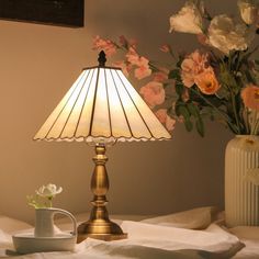 a lamp sitting on top of a bed next to a vase with flowers in it