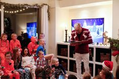 an older man standing in front of a group of children wearing pajamas and holding a tablet