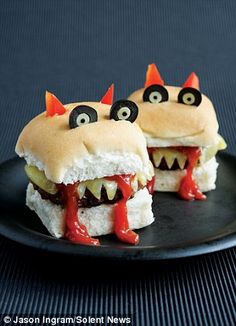 two sandwiches with monster eyes on them sitting on a black plate, ready to be eaten