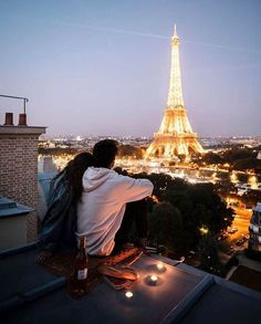 a man and woman sitting on top of a roof looking at the eiffel tower