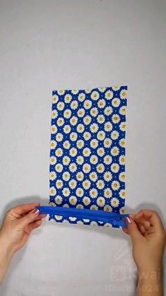 two hands holding up a small blue and white flowered notebook with yellow daisies on it