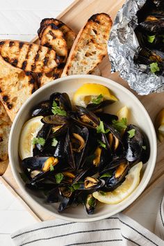 a white bowl filled with mussels and lemon wedges next to grilled bread