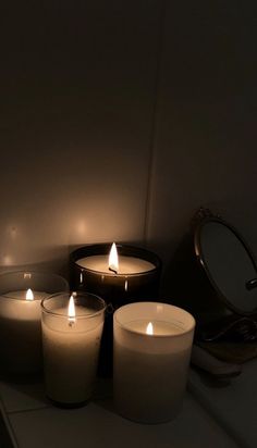 three lit candles sitting on top of a counter next to a mirror and an oval object