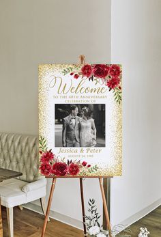 a wedding welcome sign with red flowers on it next to a white couch and wooden easer