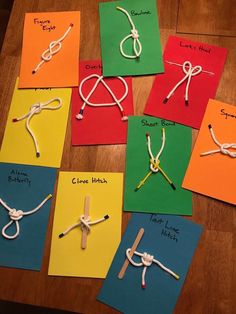 several different colored paper pieces with ropes and knots attached to them on top of a wooden table