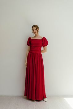 a woman in a red dress standing against a white wall with her hands on her hips