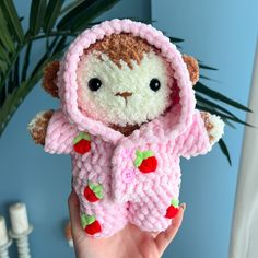 a hand holding a small stuffed animal in a knitted pink outfit with strawberry accents