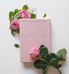 a pink book sitting on top of a table next to some flowers and greenery