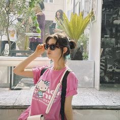 a woman in a pink shirt is holding her hand up to her face while walking down the street