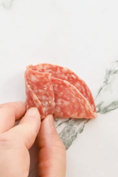 a person holding some meat in their hand on a marble counter top with grey veining