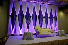 the stage is set up for an event with purple lights and drapes on it