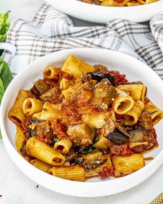 two white bowls filled with pasta and sauce on top of a table next to bread