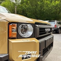 the front end of a yellow truck parked in a parking lot next to other cars