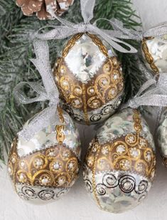 five ornaments are hanging from a christmas tree with pine cones in the foreground and snow on the ground behind them