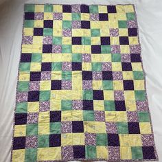 a yellow and green quilt is laying on a white bed sheet that has been made to look like a checkerboard pattern