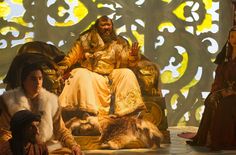 two people dressed in medieval costumes sitting on a stage with an animal statue behind them