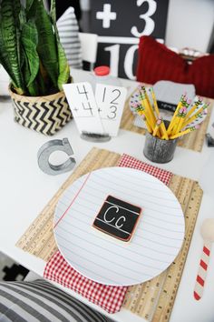 a white table topped with lots of paper and pencils next to a potted plant