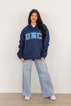 a woman standing in front of a white wall wearing an unc sweatshirt and wide jeans