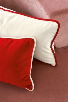 two red and white pillows sitting on top of a pink couch next to each other