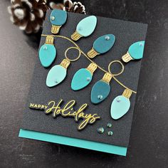 a handmade christmas card with blue and gold ornaments hanging from it's sides