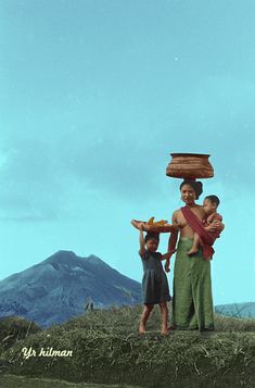 two people with baskets on their heads are standing in the grass and mountains behind them