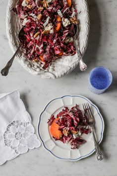 a white bowl filled with red cabbage and carrots next to a plate of food