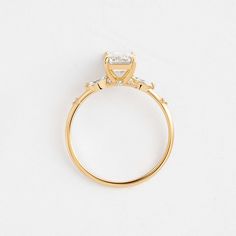 a yellow gold ring with a princess cut diamond set in the center and side stones