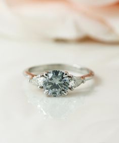 an engagement ring with three stones on it and a flower in the backgrouf