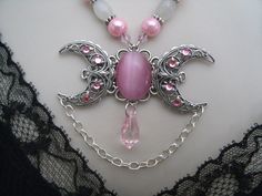 "This beautiful necklace has a pink catseye stone set on a sterling silver plated triple moon pendant with rhinestones and moonstone beads, pewter silver accent beads, pink Czech glass beads and pink pearl beads. 18\" long. Toggle clasp." Handmade Pink Moonstone Jewelry, Handmade Mystical Pink Jewelry, Pink Mystical Handmade Jewelry, Pink Handmade Mystical Jewelry, Pink Moon Charm Jewelry, Handmade Pink Gothic Jewelry, Pink Round Moon Charm Jewelry, Pink Moon-shaped Jewelry With Moon Charm, Pink Gothic Jewelry