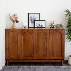 a wooden cabinet sitting next to a wall with pictures and plants on top of it