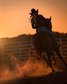 a woman riding on the back of a brown horse in an arena at sundown