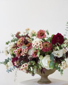 a vase filled with lots of flowers sitting on top of a white table next to a plant