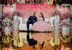 a man and woman sitting on a couch in front of a floral wall with flowers