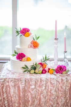 a wedding cake with flowers and candles on the table in front of a large window