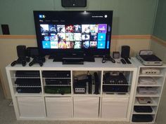 a flat screen tv sitting on top of a white entertainment center next to shelves filled with electronics