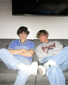 two young men sitting on top of a couch next to each other in front of a flat screen tv