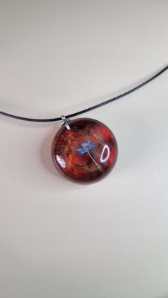 a necklace with a red glass bead hanging from a black cord on a white surface