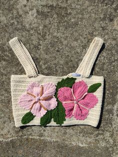 a crocheted purse with pink flowers and green leaves on the front, sitting on a stone surface