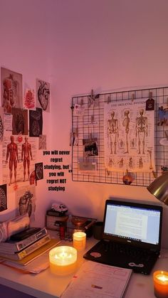 a laptop computer sitting on top of a desk next to a lit candle and some pictures