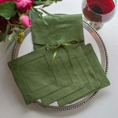 two napkins tied together on a plate next to a glass of wine and flowers