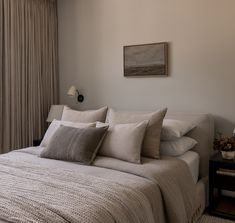 a bed with white sheets and pillows in a bedroom next to a wall mounted painting