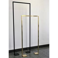 two tall black and gold metal stands against a white wall, one standing on its own legs